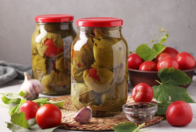 Gemarineerde tomaten met knoflook in druivenbladeren in twee glazen potten op grijze muur. Detailopname. Horizontaal formaat