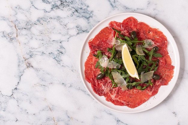 Foto gemarmerde rundercarpaccio met rucola kappertjes citroen en parmezaanse kaas