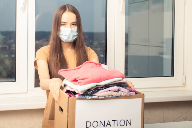 Gemaskerd meisje met een donatiedoos met kleding voor arme mensen