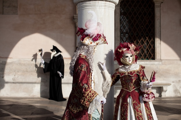 Foto gemaskerd stel in sierlijke klederdracht bij de venetiaanse maskerade staat tegen een stenen muur bij het san marcoplein in venetië