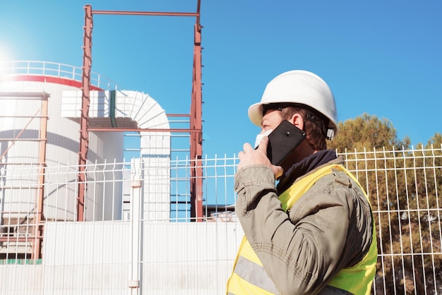 Gemaskerde bouwerMedische maskerbouwvakker op het grondgebied van een industriële onderneming spreekt aan de telefoonArbeidersinspecteur in uniform in industrieobject