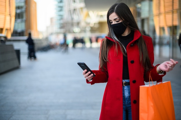 Gemaskerde jonge vrouw die in een stad loopt terwijl ze haar mobiele telefoon gebruikt