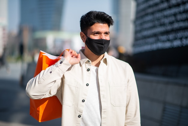 Gemaskerde jongeman die boodschappentassen draagt terwijl hij een masker, covid en coronavirusconcept draagt