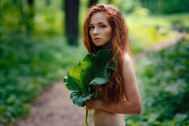 Gember mooie vrouw met een groot verlof over haar borst zonder kleren eronder in een bos