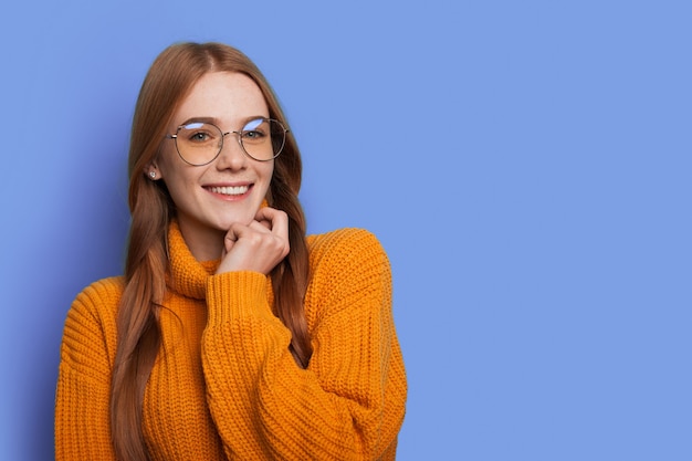 Gember vrouw met rood haar lacht naar camera met bril op een blauwe studiomuur met vrije ruimte