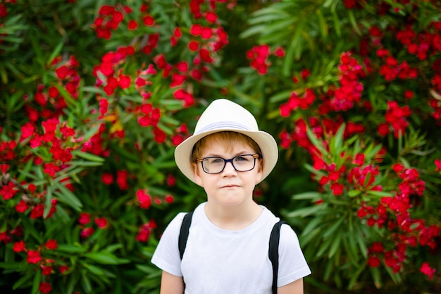 Gemberjongen in de strohoed en grote glazen dichtbij de groene struik met rode bloemen in het de zomerpark