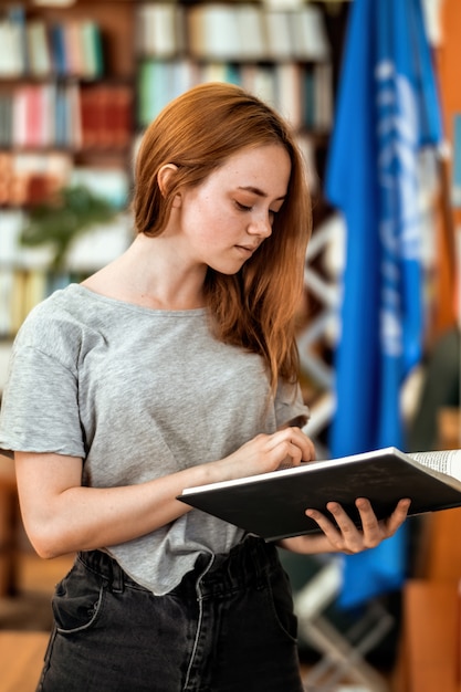 Gembermeisje dat met vrijetijdskleding naar oude boeken zoekt