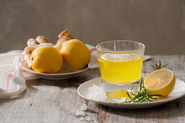 Gemberthee met citroen, gemberwortel en rozemarijn op houten tafel. Kleine glazen doorzichtige kan met warme drank.