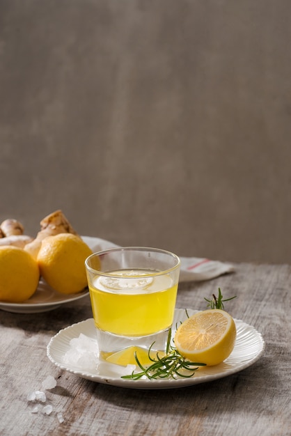 Gemberthee met citroen, gemberwortel en rozemarijn op houten tafel. Kleine glazen doorzichtige kan met warme drank.