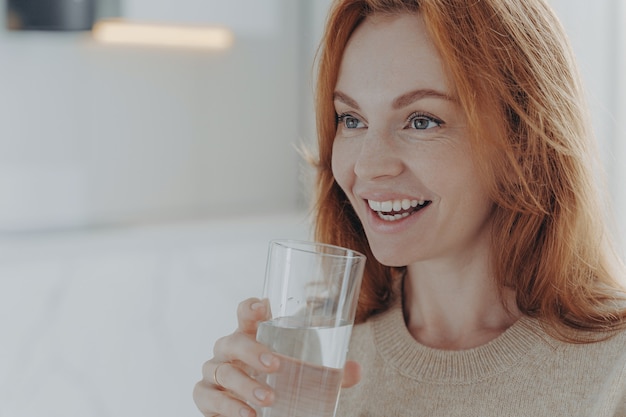 Gembervrouw drinkt zuiver water uit glas geniet van verfrissend drankje