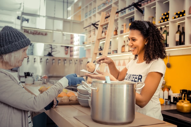 Gemeenschap helpen. Vrolijke jonge vrouw die voedsel serveert tijdens het werken in het vrijwilligerscentrum