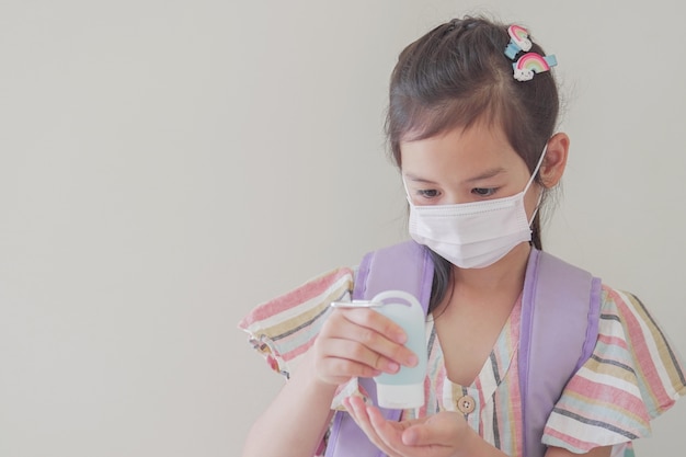 Gemengd Aziatisch meisje dat masker draagt en handdesinfecterend middel, terug naar schoolconcept toepast