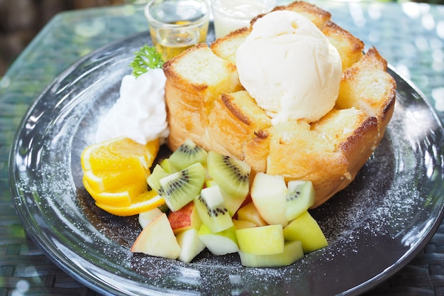 Gemengd fruit en honing toast met ijs in zwarte schotel op tafel