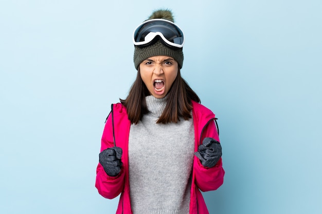 Gemengd ras skiër meisje met snowboard bril over geïsoleerde blauwe muur gefrustreerd door een slechte situatie