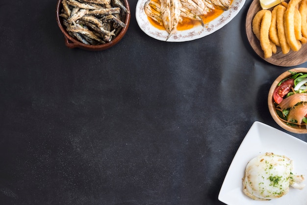 Gemengd van vis (inktvis, gebakken sardines, salade met zalm) op zwarte achtergrond