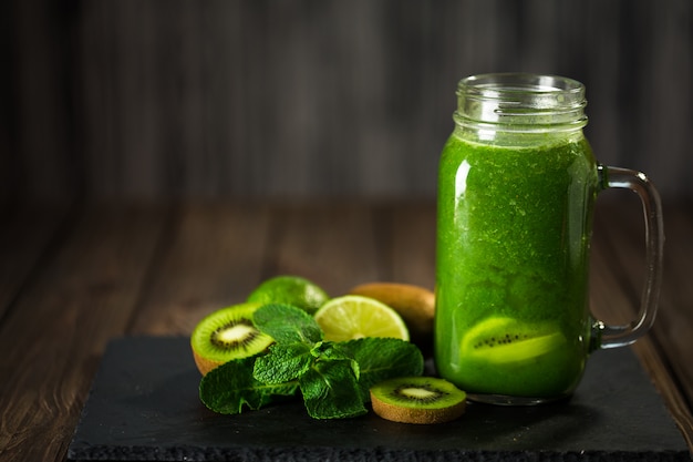 Gemengde groene smoothie met ingrediënten op het stenen bord, houten tafel