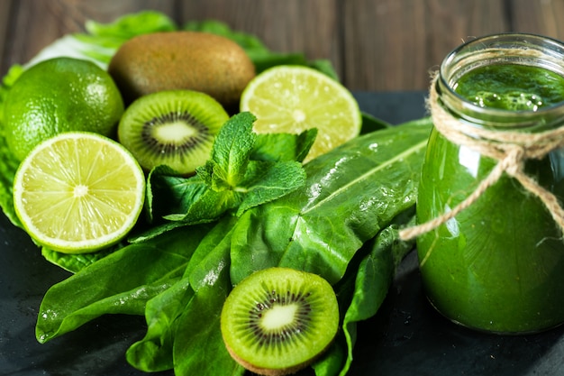 Gemengde groene smoothie met ingrediënten op het stenen bord, houten tafel