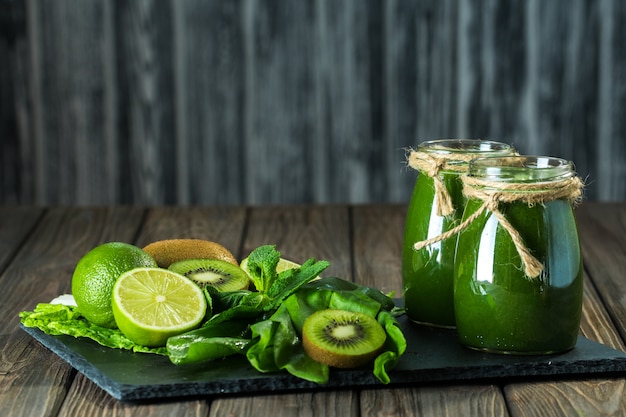 Gemengde groene smoothie met ingrediënten op het stenen bord, houten tafel