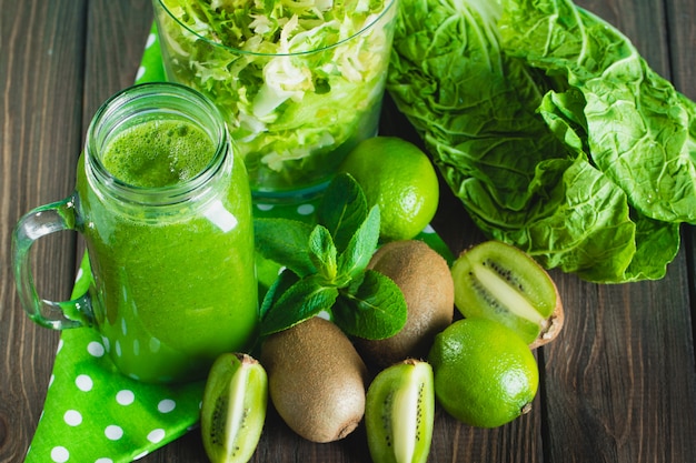 Gemengde groene smoothie met ingrediënten op houten tafel