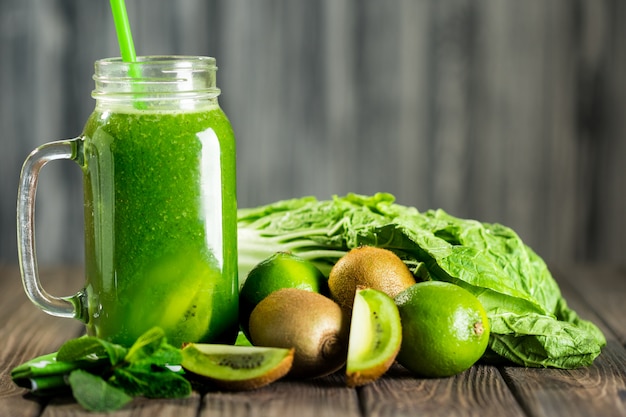 Gemengde groene smoothie met ingrediënten op houten tafel