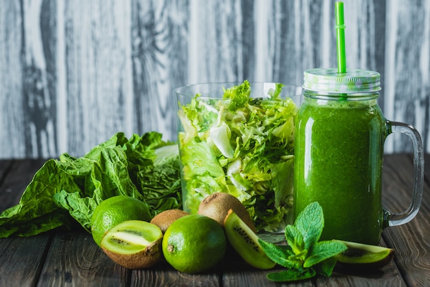 Gemengde groene smoothie met ingrediënten op houten tafel