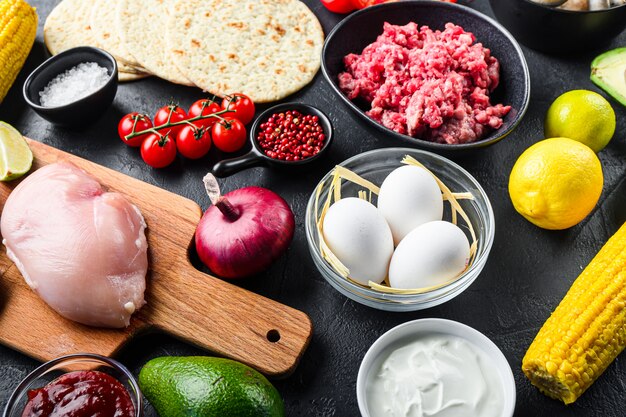 Gemengde Mexicaans eten achtergrond, rauwe biologische ingrediënten voor taco's met kip en rundvlees, maïs tortilla, salsa, Spaanse peper op zwarte achtergrond, zijaanzicht.