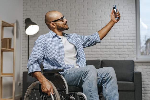 Gemengde race gehandicapte man zit in een rolstoel en gebruikt smartphone