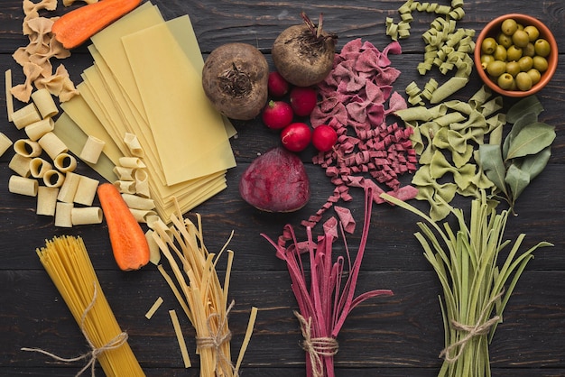 Gemengde rauwe kleurrijke Italiaanse pasta achtergrond. Handgemaakte macaroni met verschillende groenten en kruiden op donker hout, bovenaanzicht, kopieerruimte