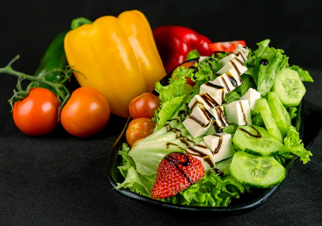 Gemengde salade met kaas en aardbei op een zwarte achtergrond met decoratieve groenten.