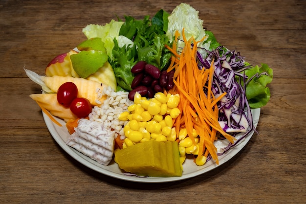 Gemengde vruchten en groentensalade in de kom op houten achtergrond