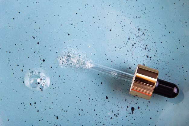 Gemorst helder serum met glazen pipet op blauwe achtergrond vloeibare cosmetische transparante productbel