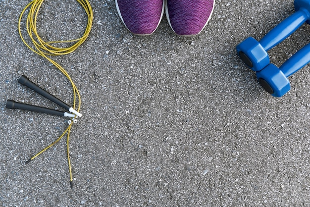 Gemotiveerd om te sporten. Twee blauwe dumpbells en springtouw liggen in de buurt van paarse sportschoenen. Fitness als hobby