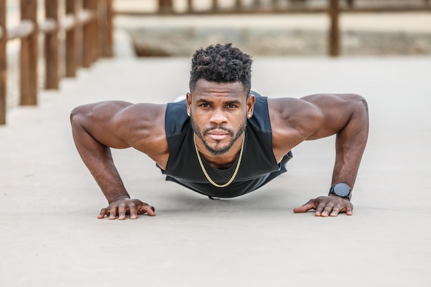 Gemotiveerde zwarte sportman die push-ups doet in het park.