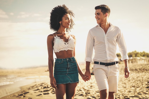 Gen z biracial paar pasgetrouwden op vakantie op het strand hand in hand wandelen