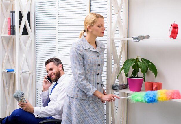 Gender concept. Gender and career. Personal assistant. Equal rights for education work and salary. Gender discrimination in business life. Woman cleaning up office while boss has phone conversation.