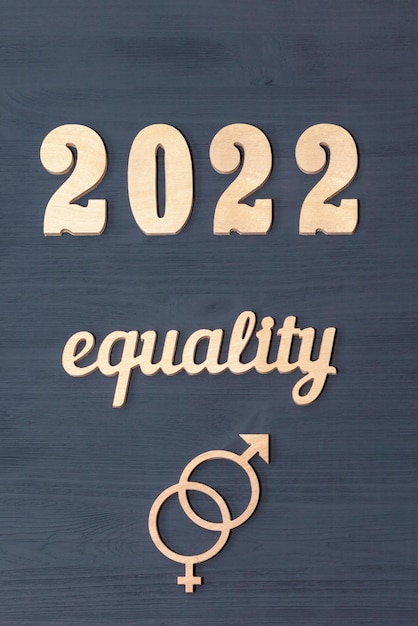 Gender equality in 2022. the word equality and the symbol of\
gender equality with the numbers 2022 carved from wood on a black\
background