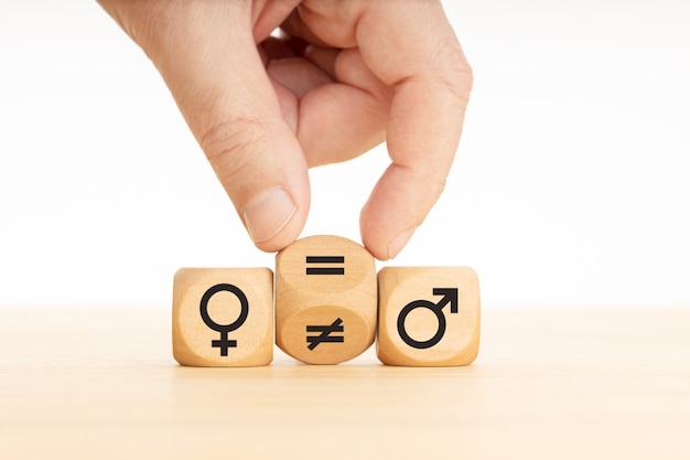 Photo gender equality concept. hand turns a wooden block and changes a unequal sign to a equal sign between symbols of men and women