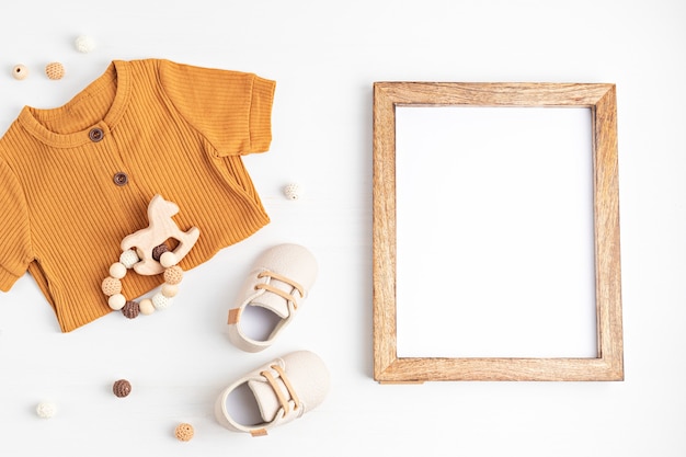 Gender neutral baby garment, accessories and empty frame. Organic cotton clothes, newborn fashion, branding, small business idea. Flat lay, top view