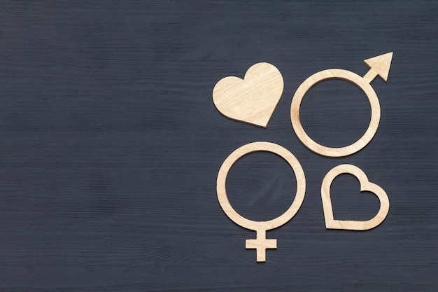 Gender symbols of men and women side by side wooden heart shape on black wooden background, copyspace