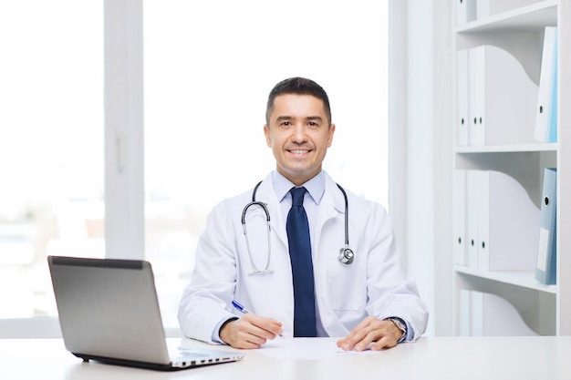 geneeskunde, beroep, technologie en mensenconcept - glimlachende mannelijke arts met laptop in medisch bureau