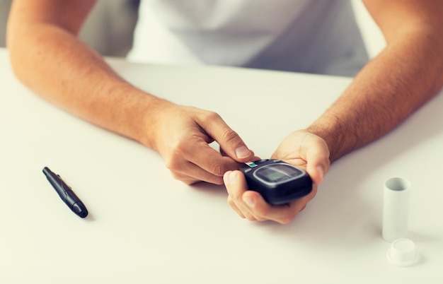 Foto geneeskunde, diabetes, glycemie, gezondheidszorg en mensenconcept - close-up van een man die zijn bloedsuikerspiegel thuis met een glucometer controleert