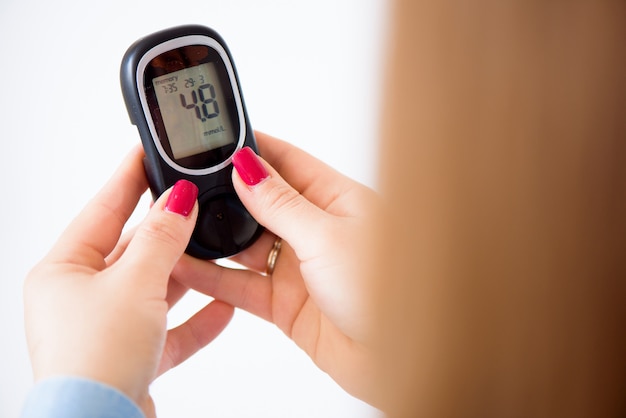 Geneeskunde, diabetes, glycemie, gezondheidszorg en mensenconcept - sluit omhoog van vrouw die bloedsuikerspiegel thuis controleren door glucometer