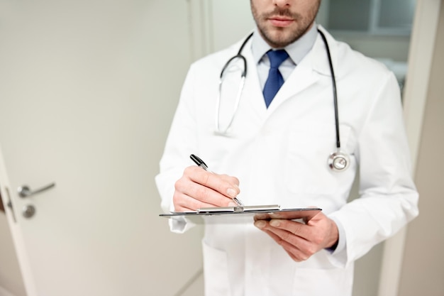 geneeskunde, gezondheidszorg, beroep en mensenconcept - close-up van mannelijke arts met klembord en stethoscoop in het ziekenhuis