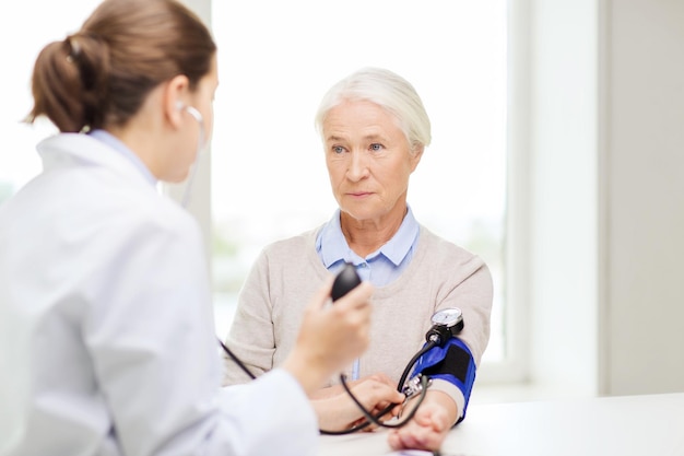 geneeskunde, leeftijd, gezondheidszorg en mensenconcept - arts die met tonometer het hogere bloeddrukniveau van de vrouw in het ziekenhuis controleert