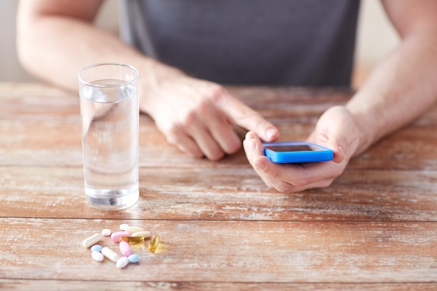 Geneeskunde, technologie, voedingssupplementen en mensenconcept - close-up van mannelijke handen smartphone, pillen en water op tafel