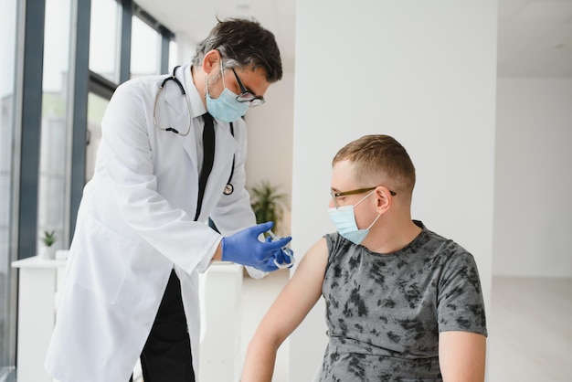 Geneeskundevaccinatie en gezondheidszorgconcept arts die gezichtsbeschermend medisch masker draagt voor bescherming tegen virusziekte met spuit die injectie van vaccin aan mannelijke patiënt doet