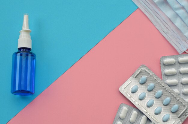Geneesmiddelen op een roze blauwe achtergrond pillen een medisch masker en een fles met druppels