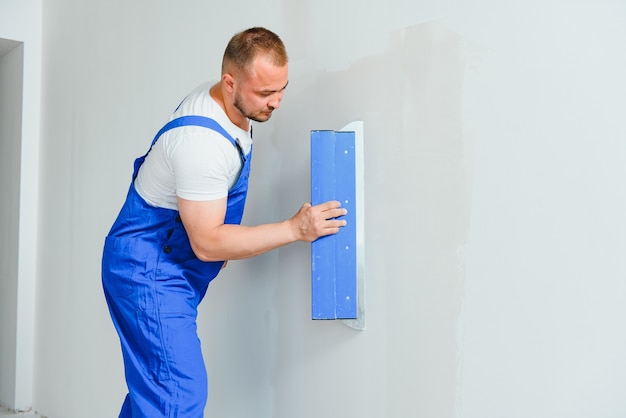 A general laborer in overalls uses a trowel to cover the wall with cement