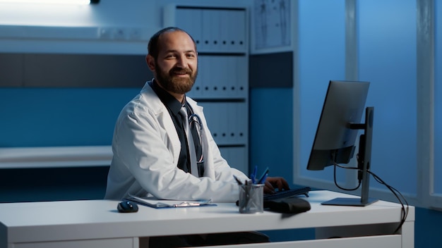 General practitioner doctor sitting at desk working late at night at patient diagnosis expertise typing medical report on computer in hospital office. Nurse planning health care treatment