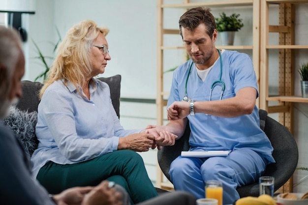 Photo general practitioner looking at wristwatch while taking pulse of a senior woman during a home visit